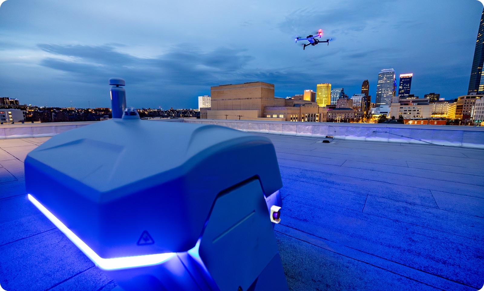 An AERROSECURITTAS autonomous launch nest on a rooftop at dusk, an airframe airborne above the city skyline
